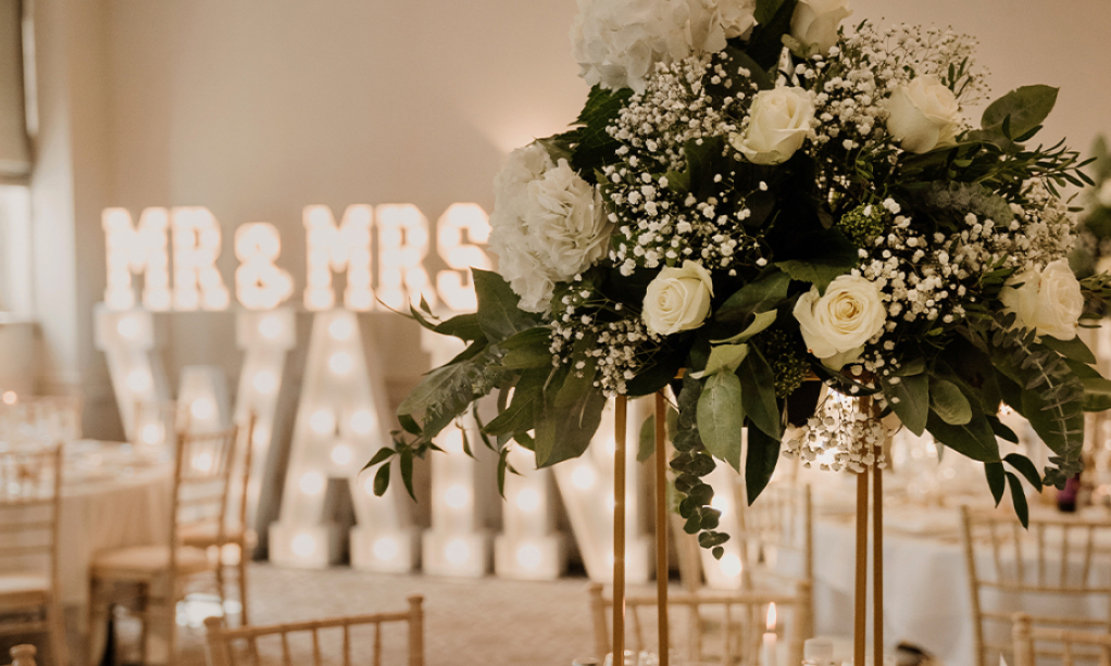 Wedding florals on table with light-up letters in background.